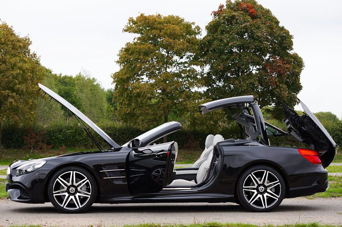 Sleek black convertible car with open doors and roof on a scenic road.
