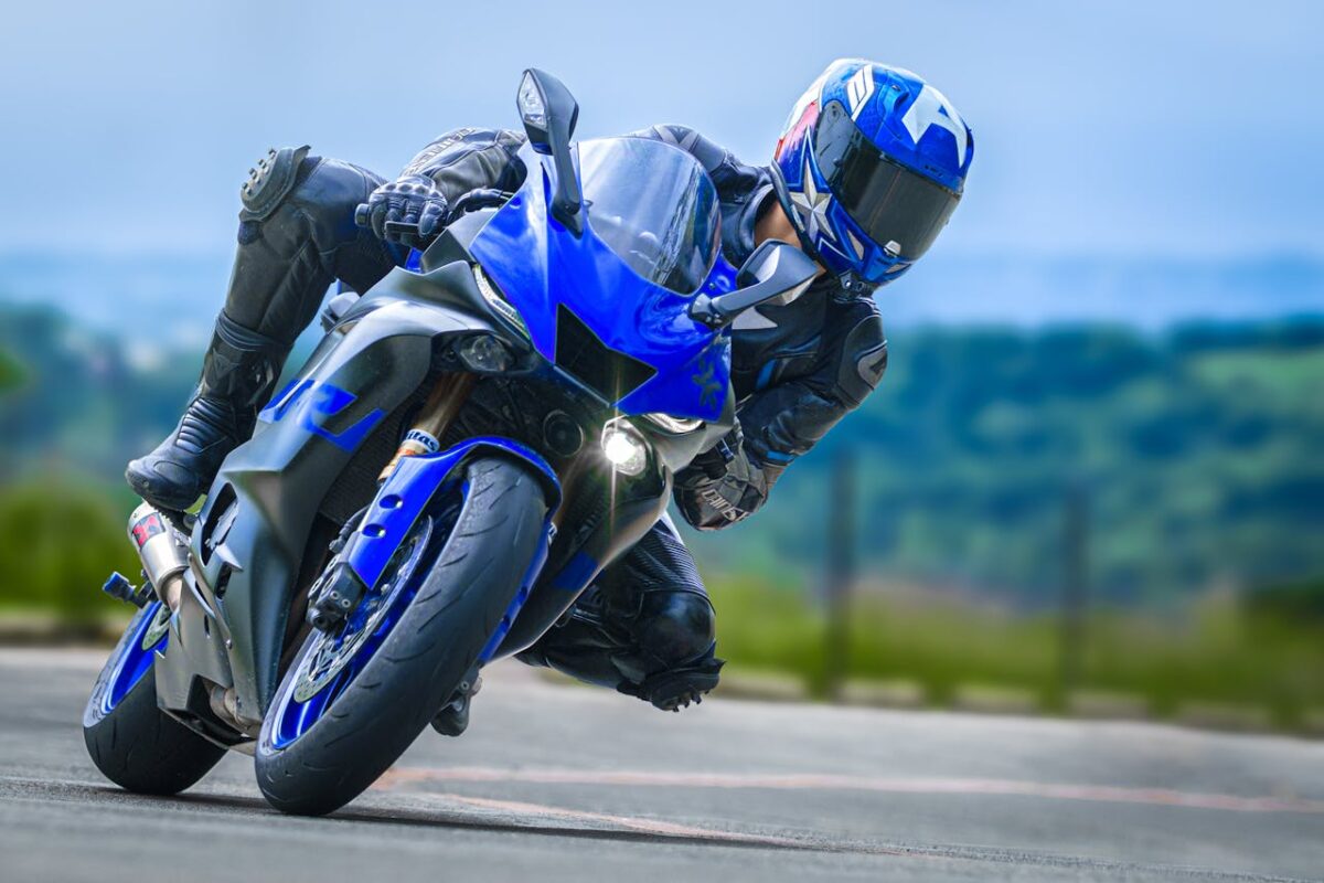 Motorcycle racer in protective gear taking a sharp turn on a sportbike. High-speed motorsport action captured outdoors.